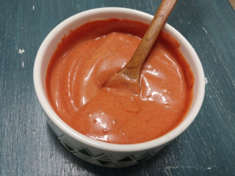 Creamy gochujang mayo sauce in white bowl with wooden spoon, showing smooth texture and coral color