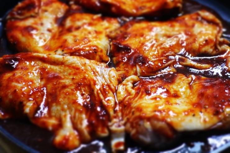 Grilled chicken thighs with caramelized Korean gochujang marinade showing glossy surface in cast iron pan