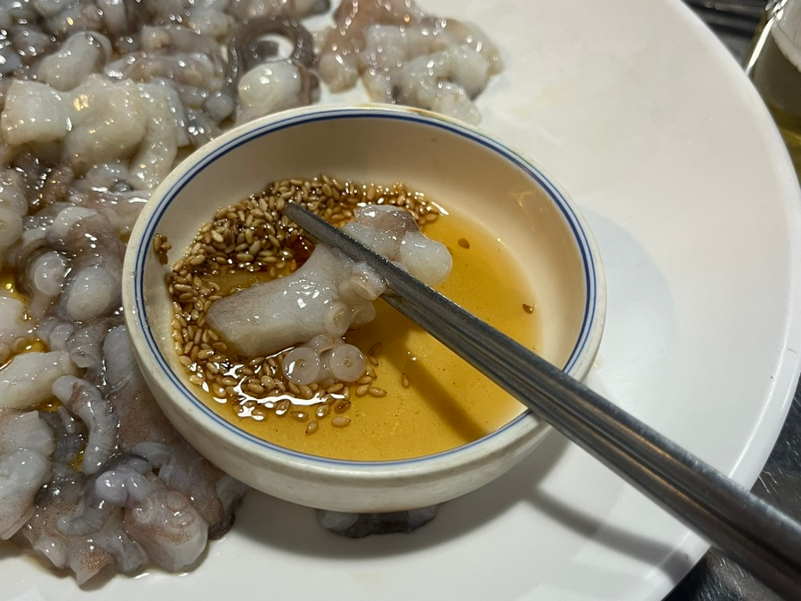 How to eat sannakji safely - dipping octopus piece in sesame oil and salt sauce with chopsticks