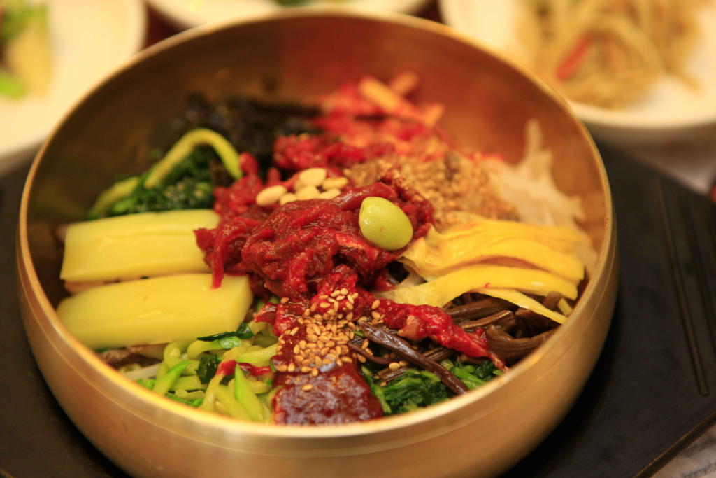 Traditional Jeonju bibimbap rice bowl with colorful vegetables, beef, and gochujang sauce in brass bowl