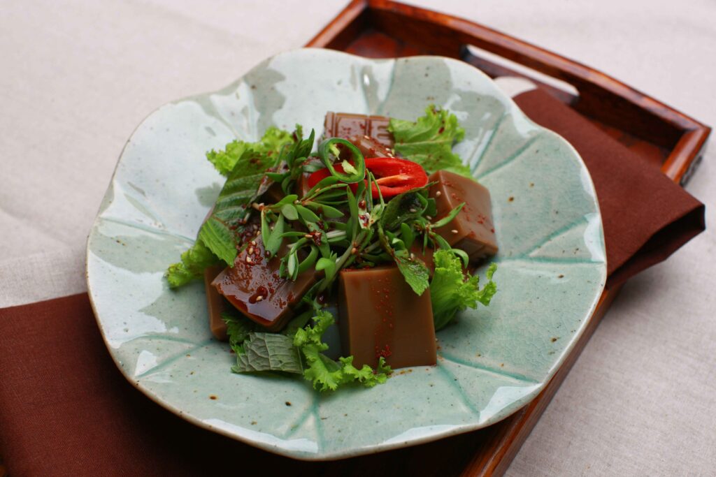 Dotorimuk muchim (Korean acorn jelly salad) with fresh greens, perilla leaves, and red chili on a traditional ceramic plate