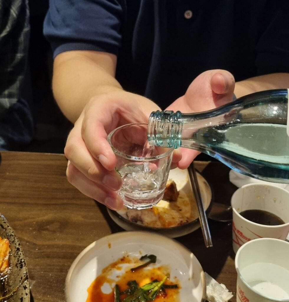 Someone pouring soju into a shot glass at a Korean restaurant, reflecting the tradition of pouring for others