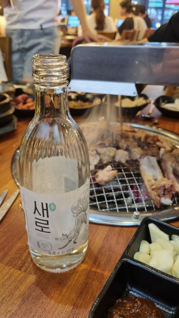 A soju bottle on a wooden table at a busy Korean barbecue restaurant