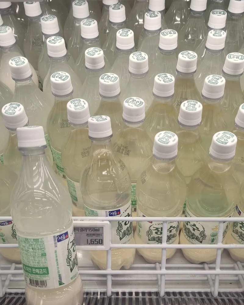 Bottles of Jangsu makgeolli in a Korean store refrigerator, each showing settled white sediment, with a price tag reading 1,650 won 