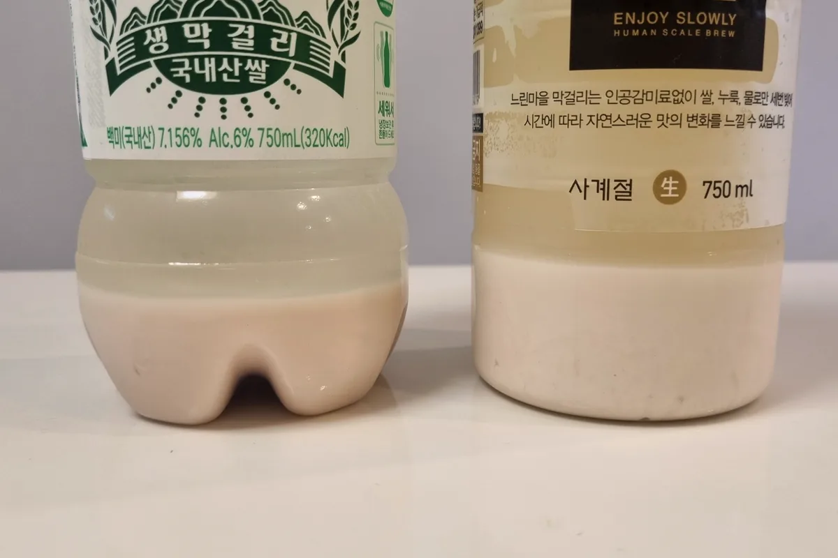 Two bottles of unpasteurized Korean makgeolli left to settle, showing a clear upper layer above thick white rice sediment