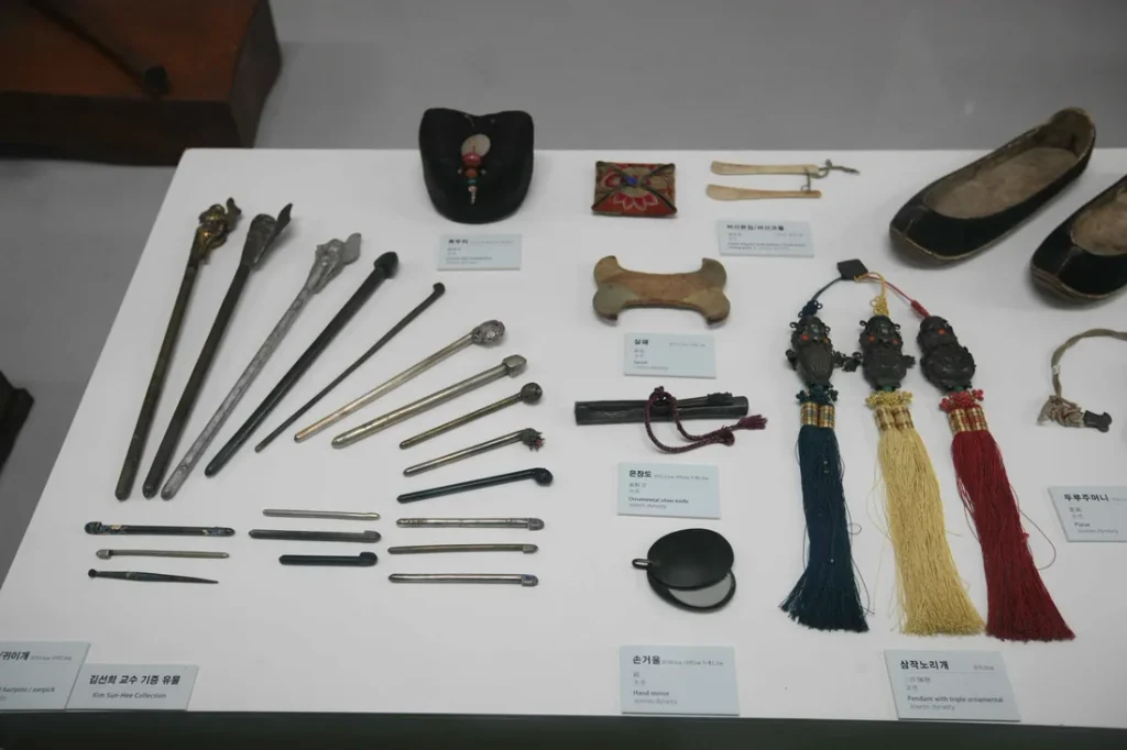 Museum display of Joseon Dynasty Korean binyeo hairpins in silver, jade, and wood, alongside a samjak norigae