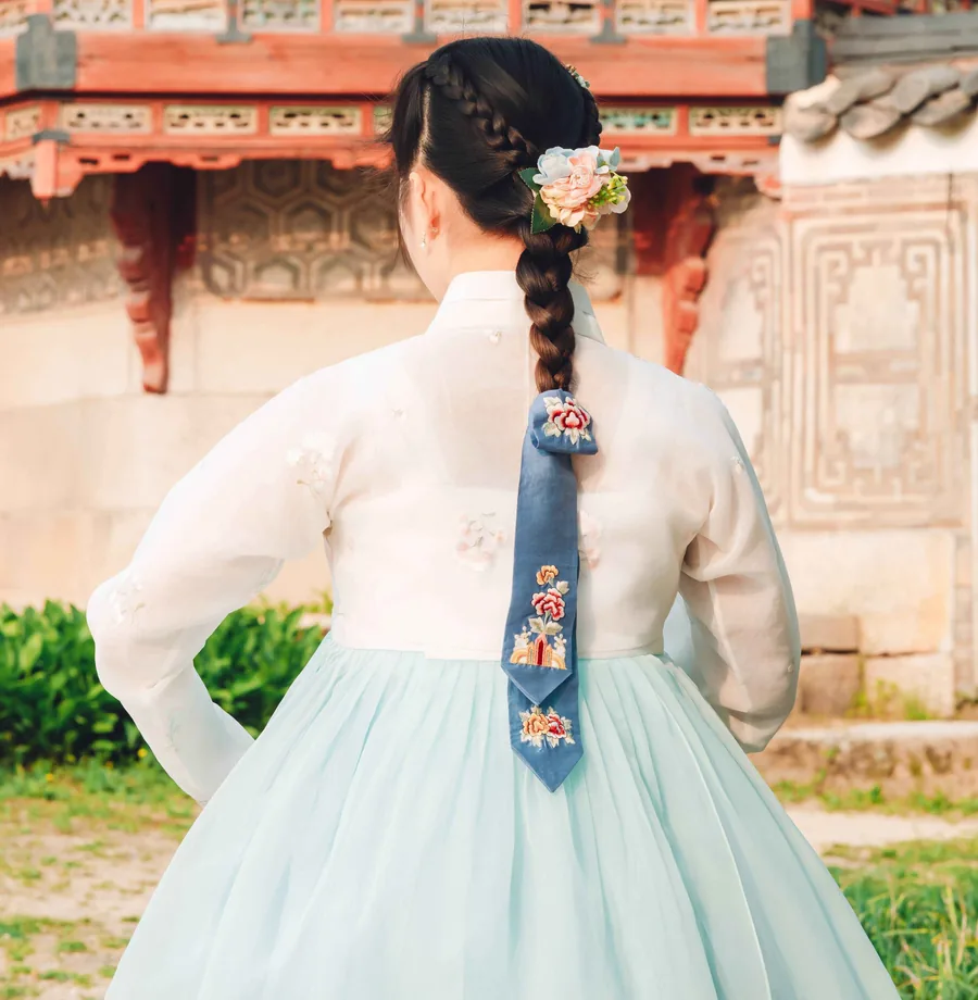 Close view of an embroidered Korean daenggi ribbon tied to a long braid, worn with hanbok