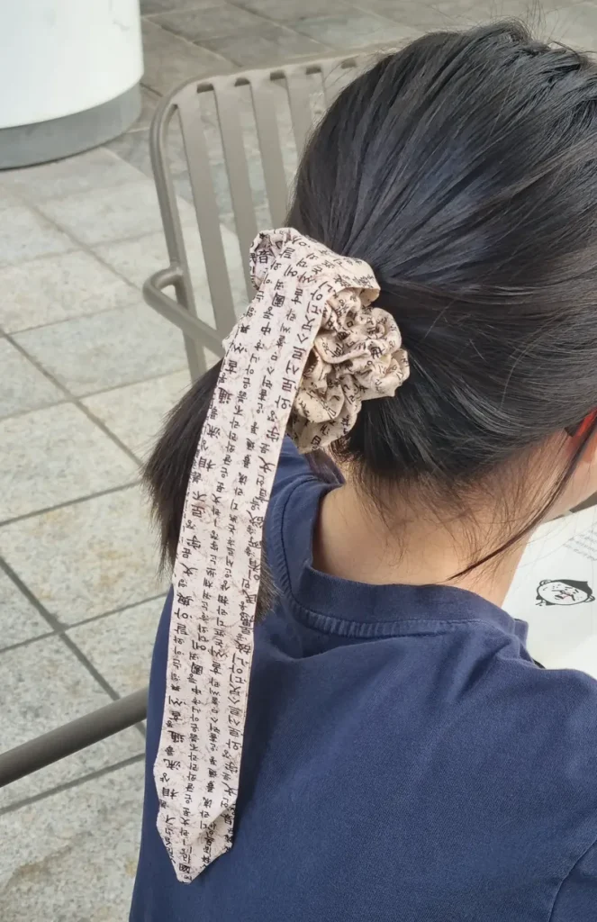 Modern Korean scrunchie with a long tail printed with Hangul manuscript text, worn in a low ponytail