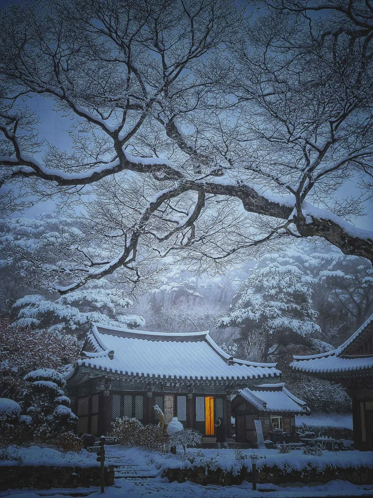 One warmly lit doorway in an otherwise dark, snow-covered temple hall at Jeondeungsa on a winter night