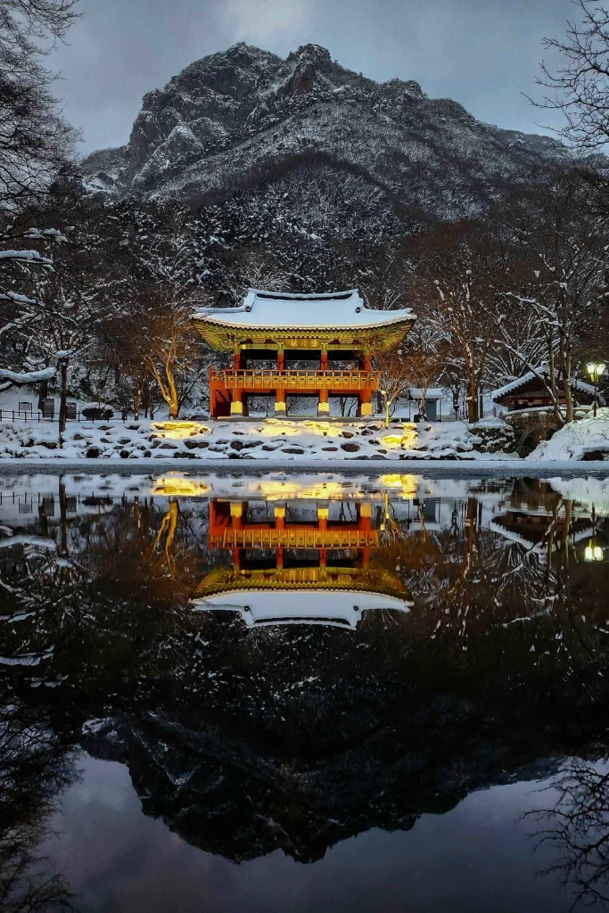 Snow-covered Ssangyeru Pavilion lit at dusk and mirrored in a still pond below Baegamsan at Baegyangsa Temple